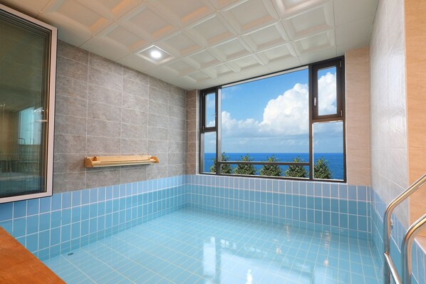 Una piscina con vista al océano, paredes con azulejos y un ventanal.
