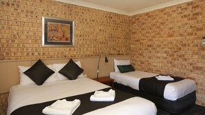 A hotel room with two beds, a brick-patterned wall, a framed artwork, and a nightstand with a lamp. - Clermont Country Motor Inn (Clermont)
