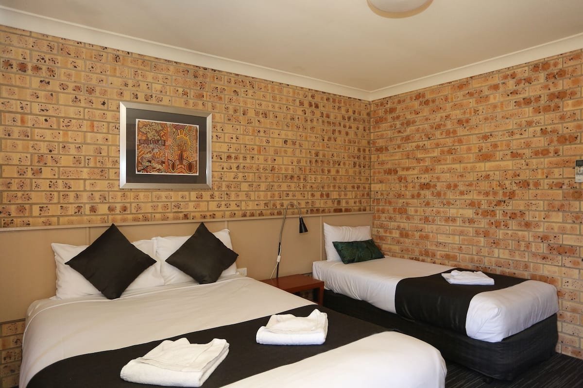 Une chambre d’hôtel avec deux lits, un mur décoré d’un motif en briques, un tableau encadré et une table de chevet avec une lampe.