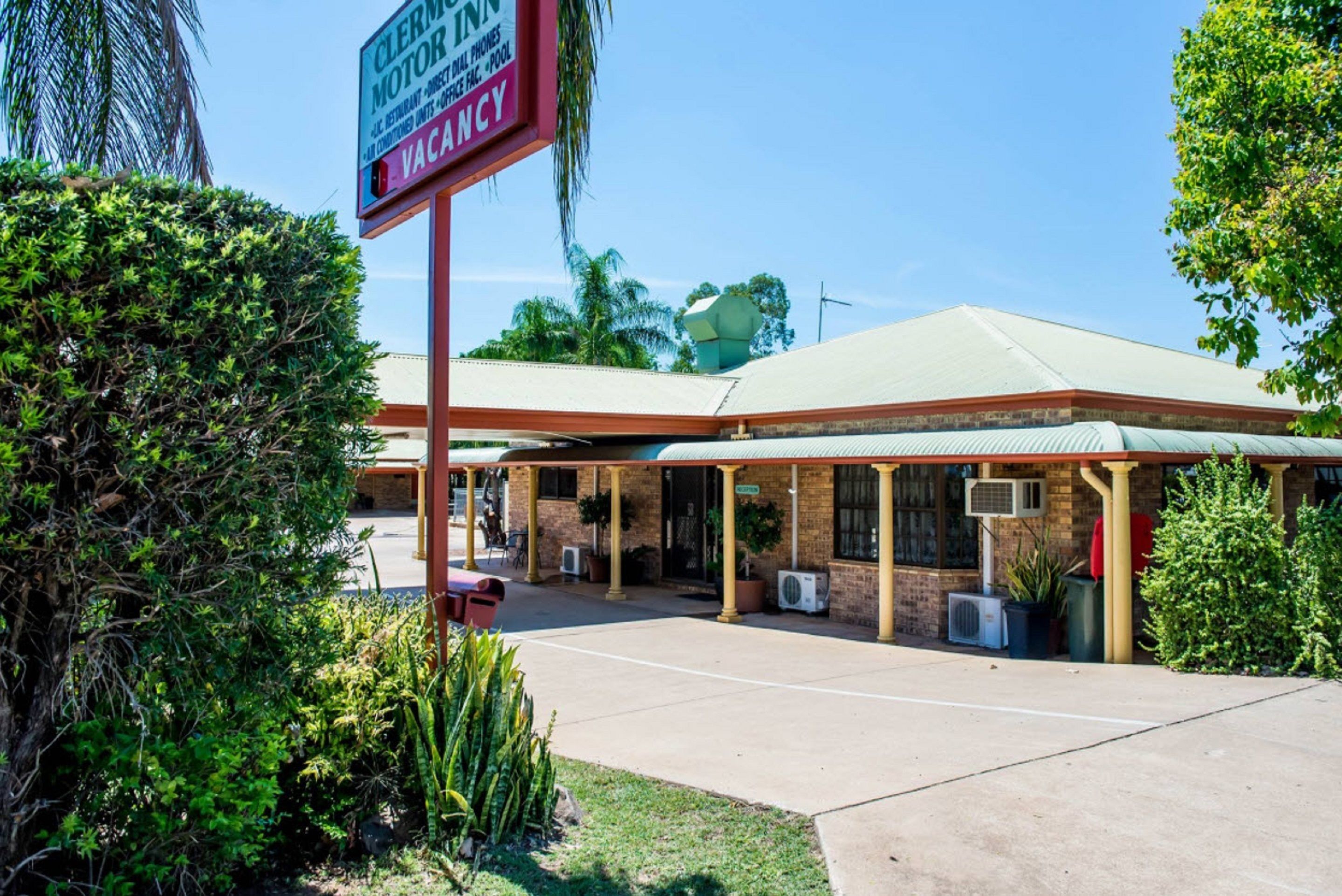 A motel with a covered parking area, air conditioning units, and a sign indicating availability.