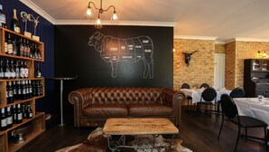 A cozy bar area with a leather couch, wooden shelves with bottles, a chalkboard with a cow diagram, and a brick wall. - Clermont Country Motor Inn (Clermont)