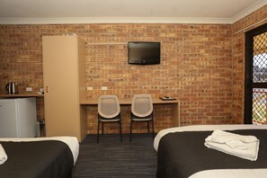 A hotel room with two beds, a desk with two chairs, a television, and a brick wall. - Clermont Country Motor Inn (Clermont)