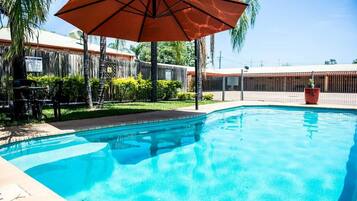 A swimming pool with a wooden fence, a patio area, and a large umbrella.