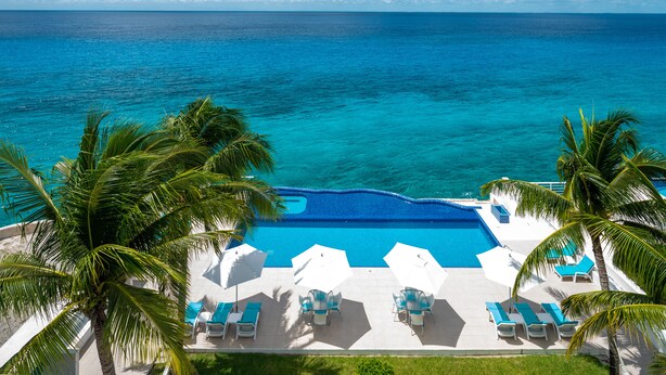 Una piscina con vista sull'oceano, circondata da palme e lettini.