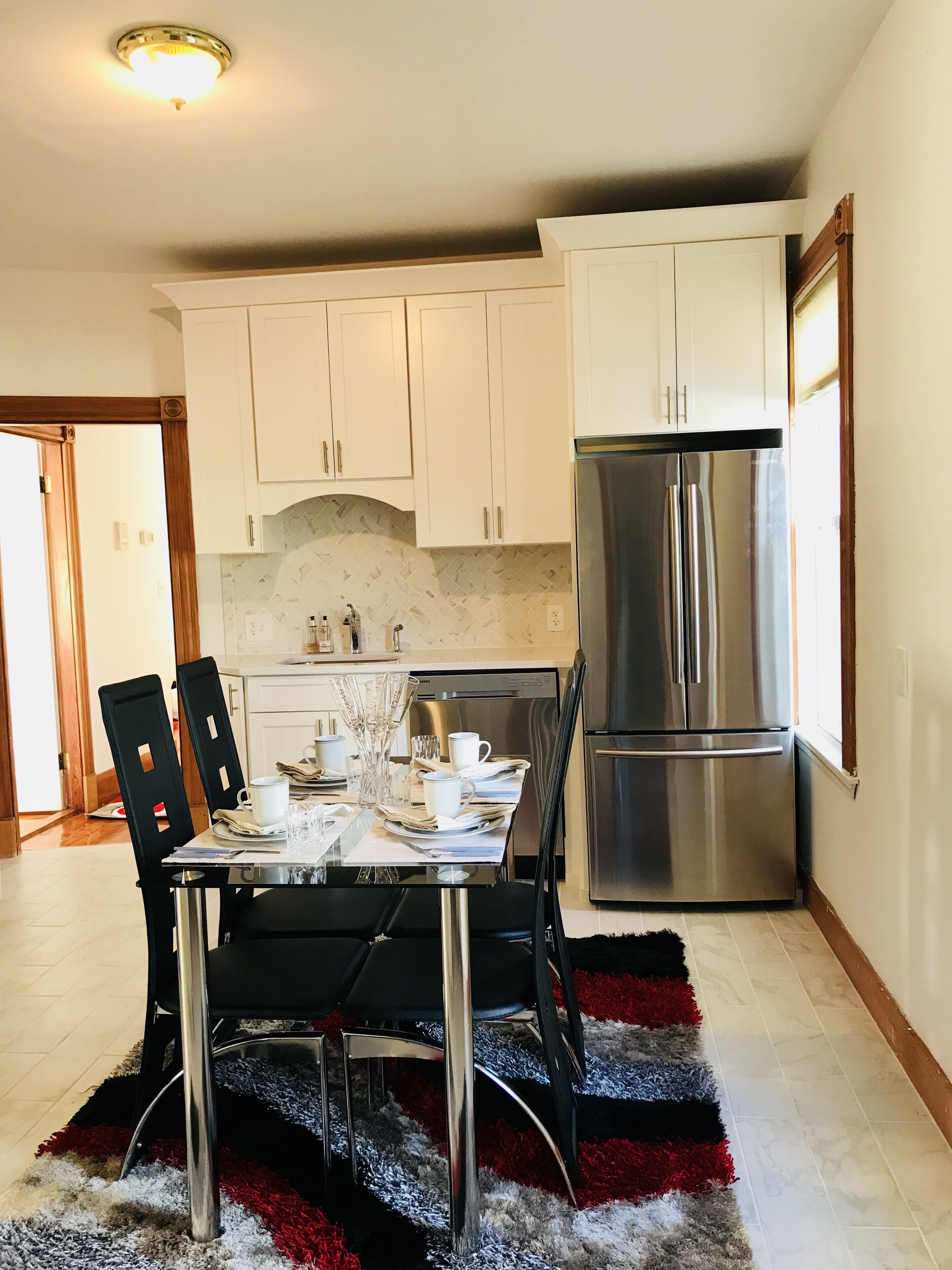 Una cocina moderna con armarios blancos, un refrigerador de acero inoxidable y una mesa de comedor con sillas.