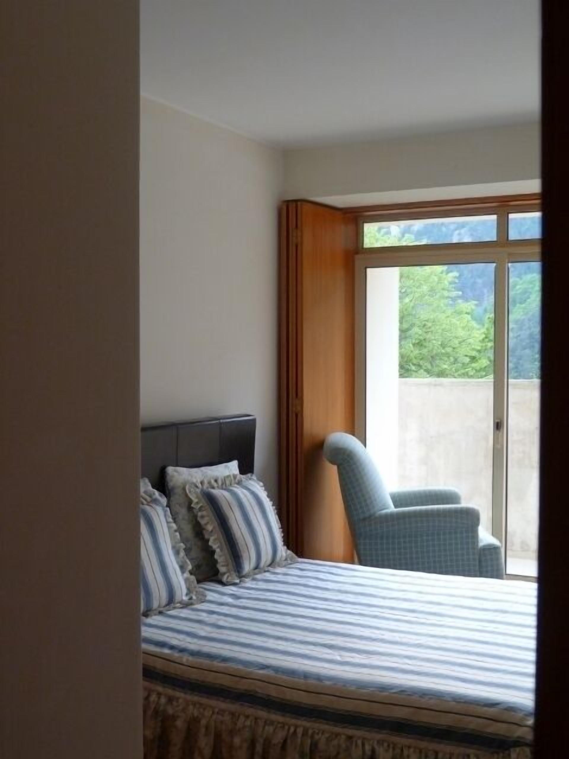 A bedroom with a bed, pillows, a chair, and a large window.