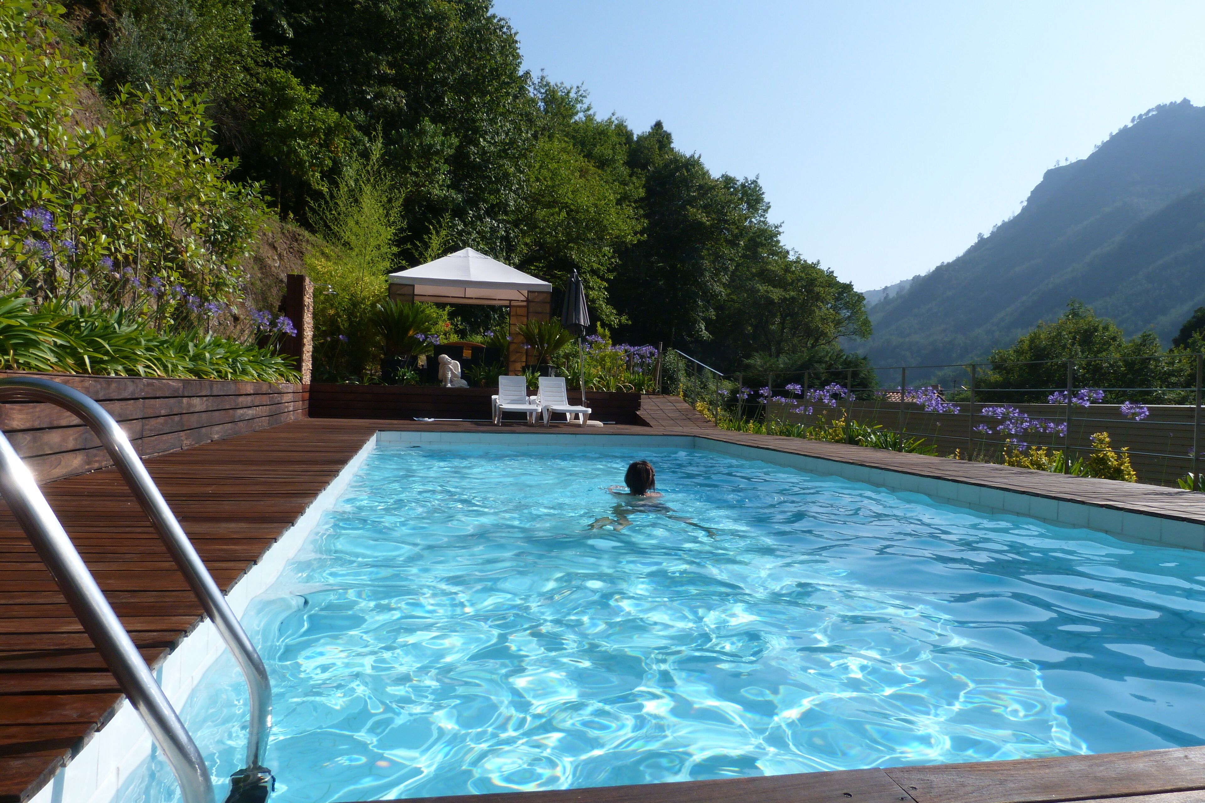En swimmingpool med træterrasse og en person, der svømmer.