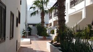A narrow courtyard with white buildings, palm trees, and potted plants. - Spacious apt with sea and pool views 2 bedrooms, wifi (Puerto del Carmen)