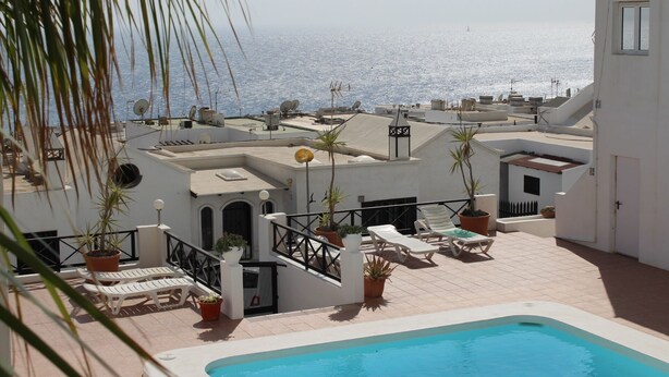A rooftop pool area with lounge chairs and potted plants, overlooking a body of water. - Spacious apt with sea and pool views 2 bedrooms, wifi (Puerto del Carmen)