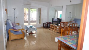 A living room with a sofa, a TV, a dining table, and a balcony door. - Spacious apt with sea and pool views 2 bedrooms, wifi (Puerto del Carmen)