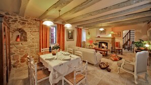 Zona pranzo con parete in pietra, travi in legno, camino e una scala.