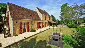 Una casa in pietra con persiane rosse, una scala in pietra e un piccolo giardino con un muretto in legno.