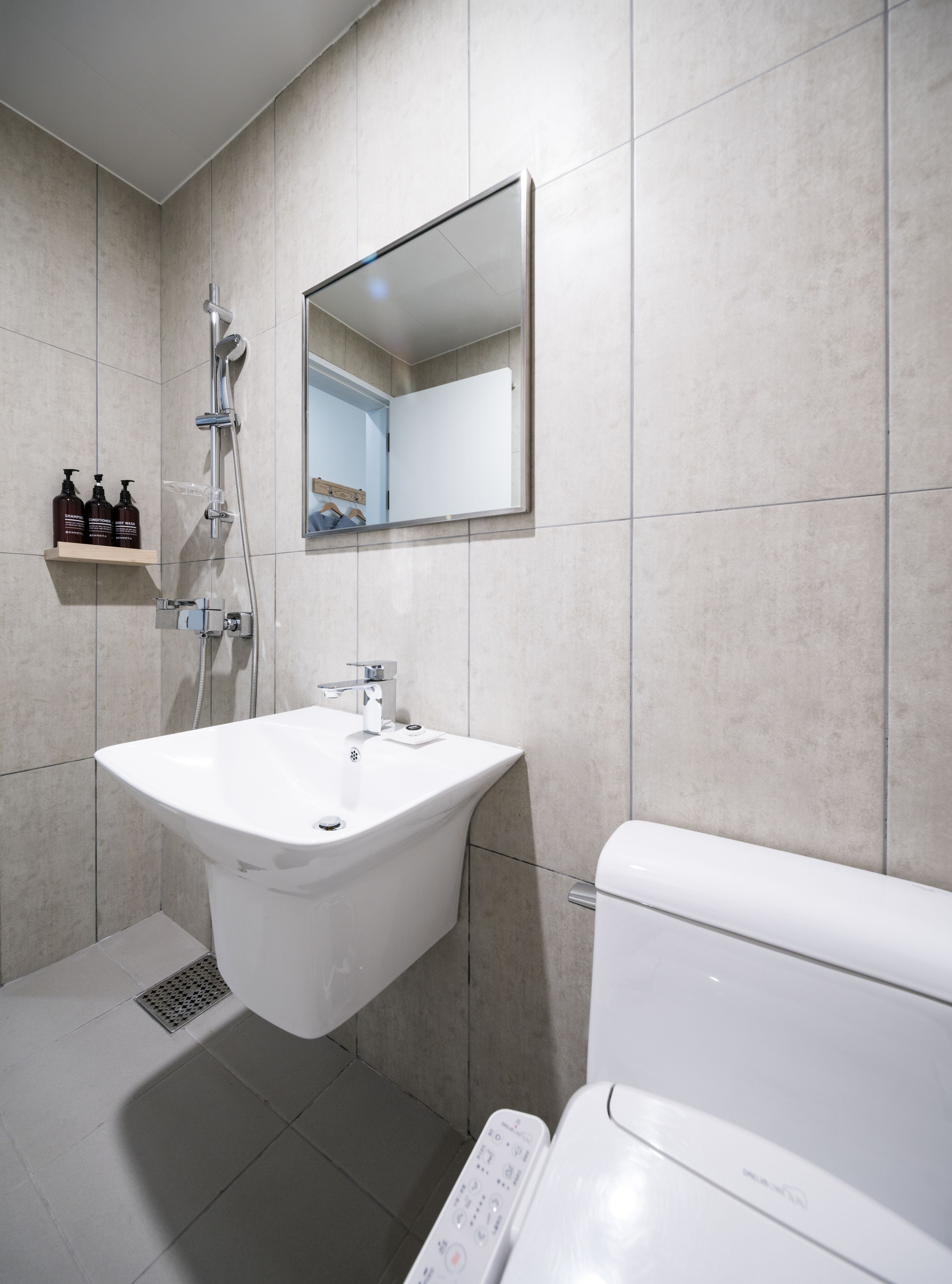 Un baño moderno con un lavamanos blanco, inodoro y ducha con cabezal de ducha manual.