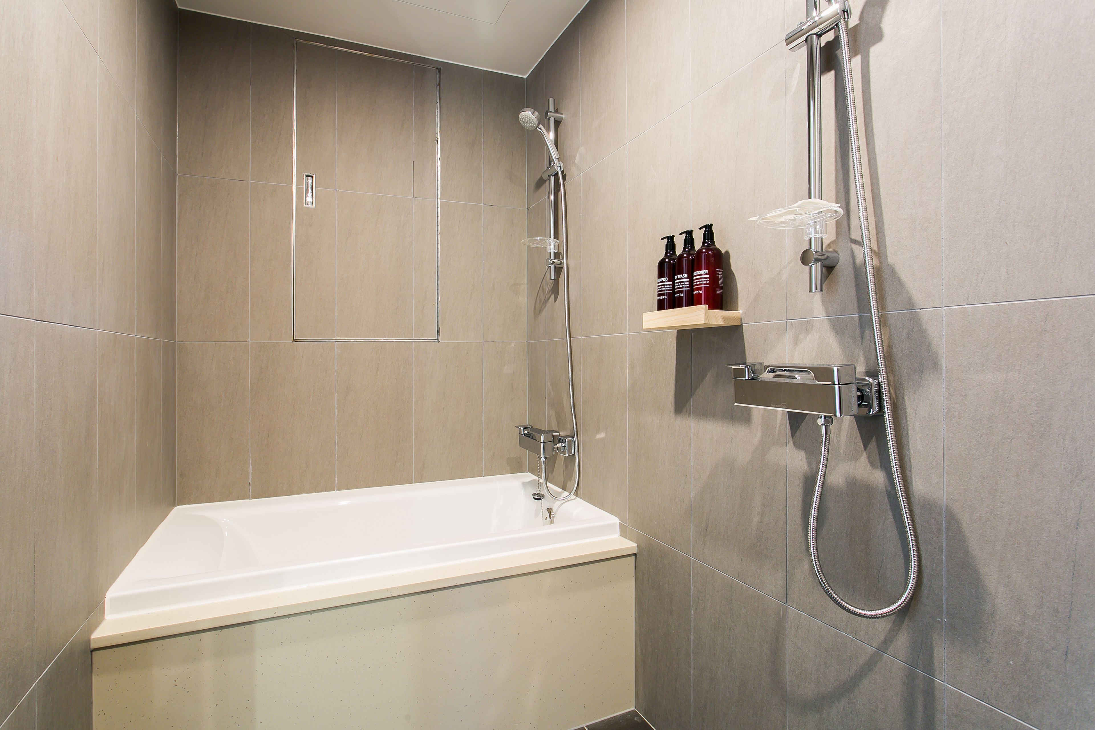 Une salle de bain moderne équipée d’une baignoire, d’une douche et d’une étagère pour les articles de toilette.