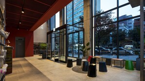 Um espaço moderno e interno, com grandes janelas, piso ladrilhado e vários taburetes pretos e verdes.