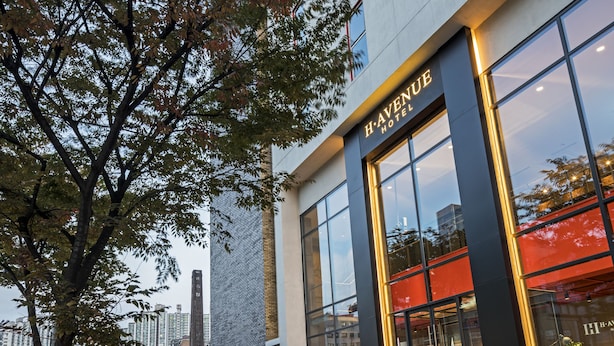 Um hotel moderno com entrada destacada, janelas amplas e uma árvore em frente.