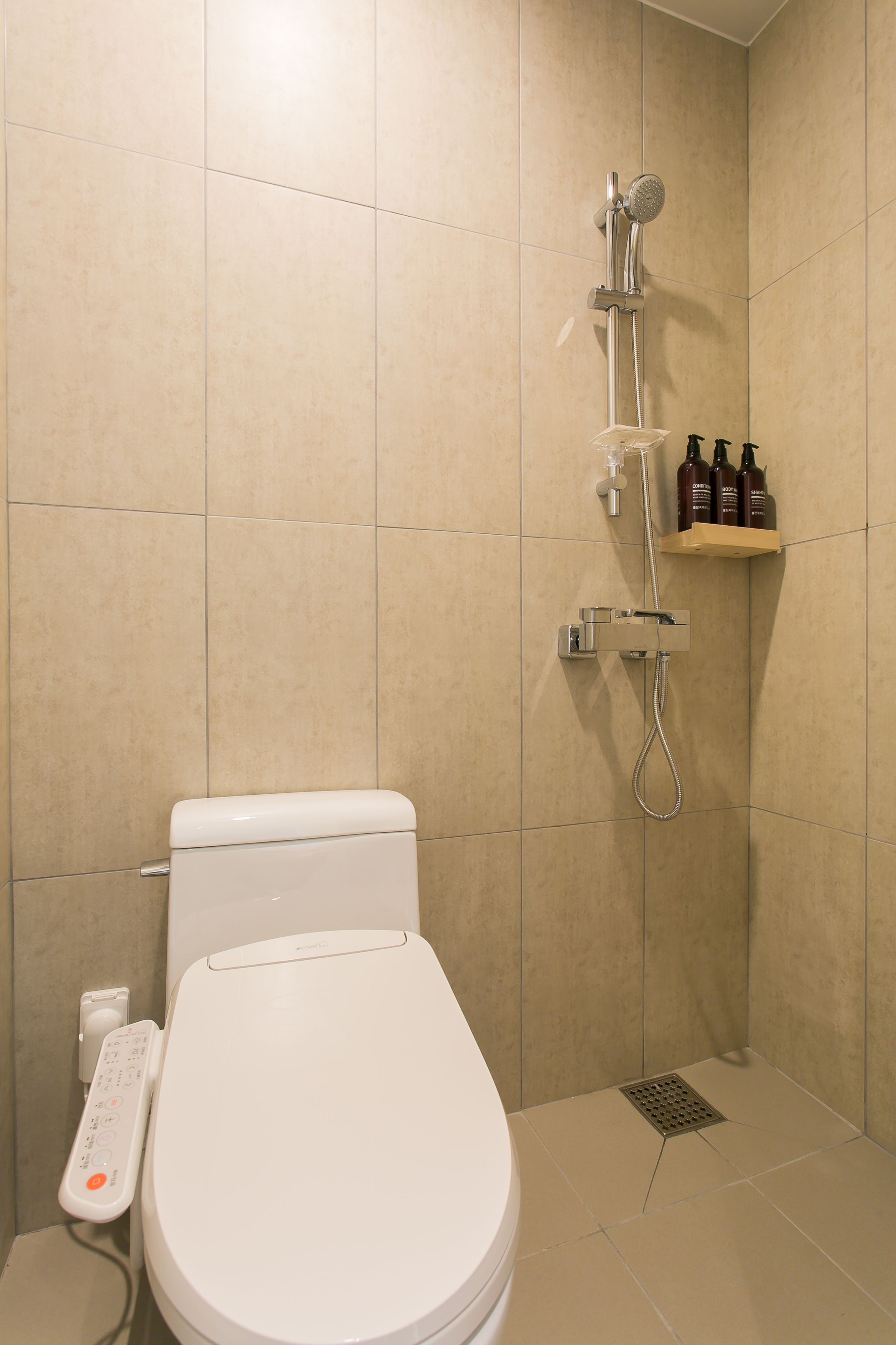 A bathroom with a toilet, a shower, and a shelf with toiletries.