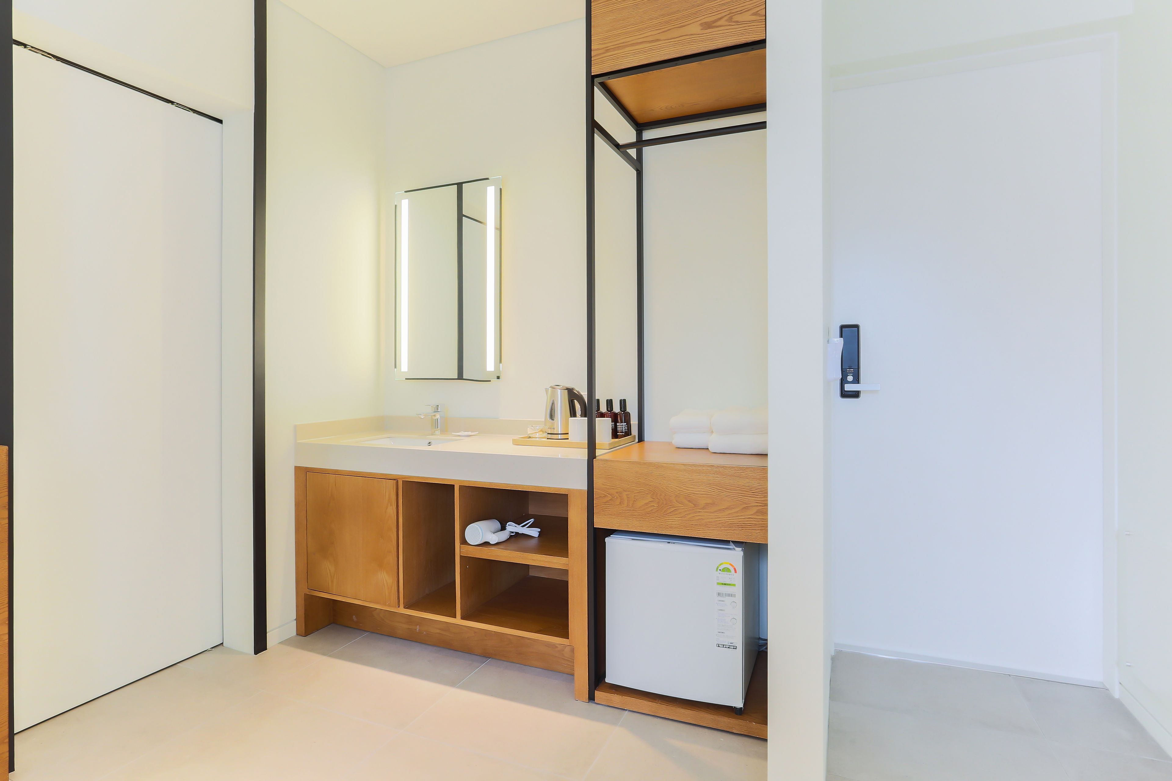 Un baño moderno con tocador de madera, espejo, lavamanos y un refrigerador pequeño.