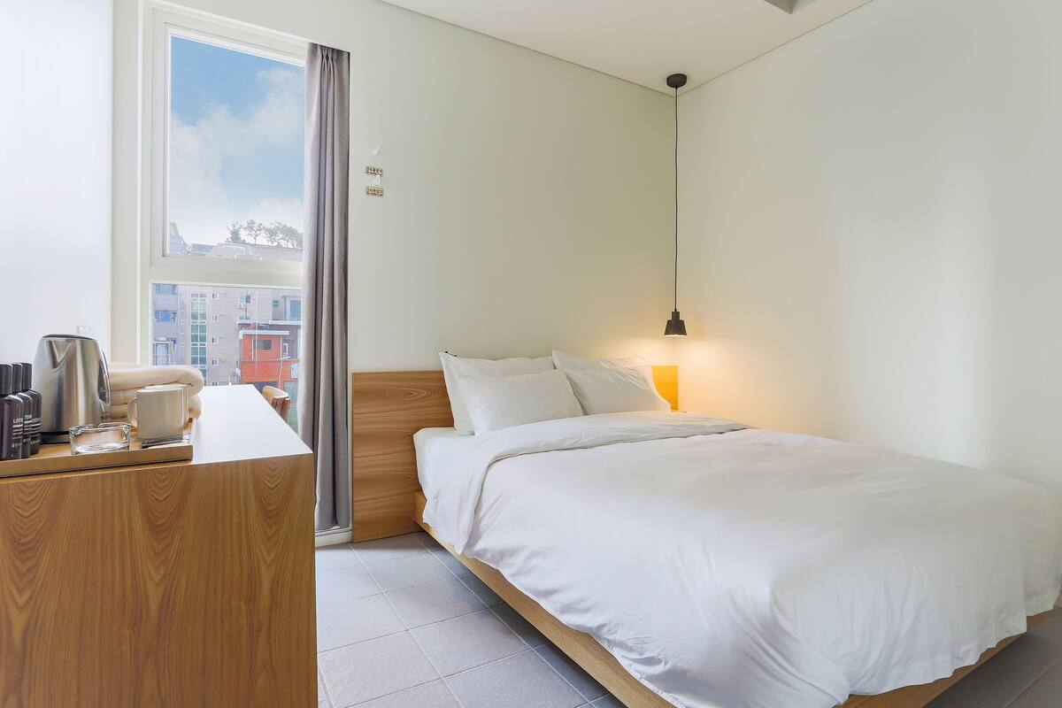A hotel room with a bed, bedside table, lamp, and a window with curtains.