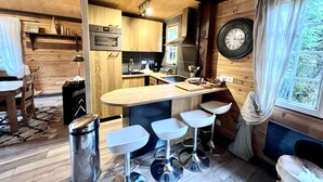 A cozy kitchen with wooden cabinets, a large clock, and a bar area with stools. - Dream cottage in the heart of nature: forest, river, cabin atmosphere & wood stove (Xonrupt-Longemer)