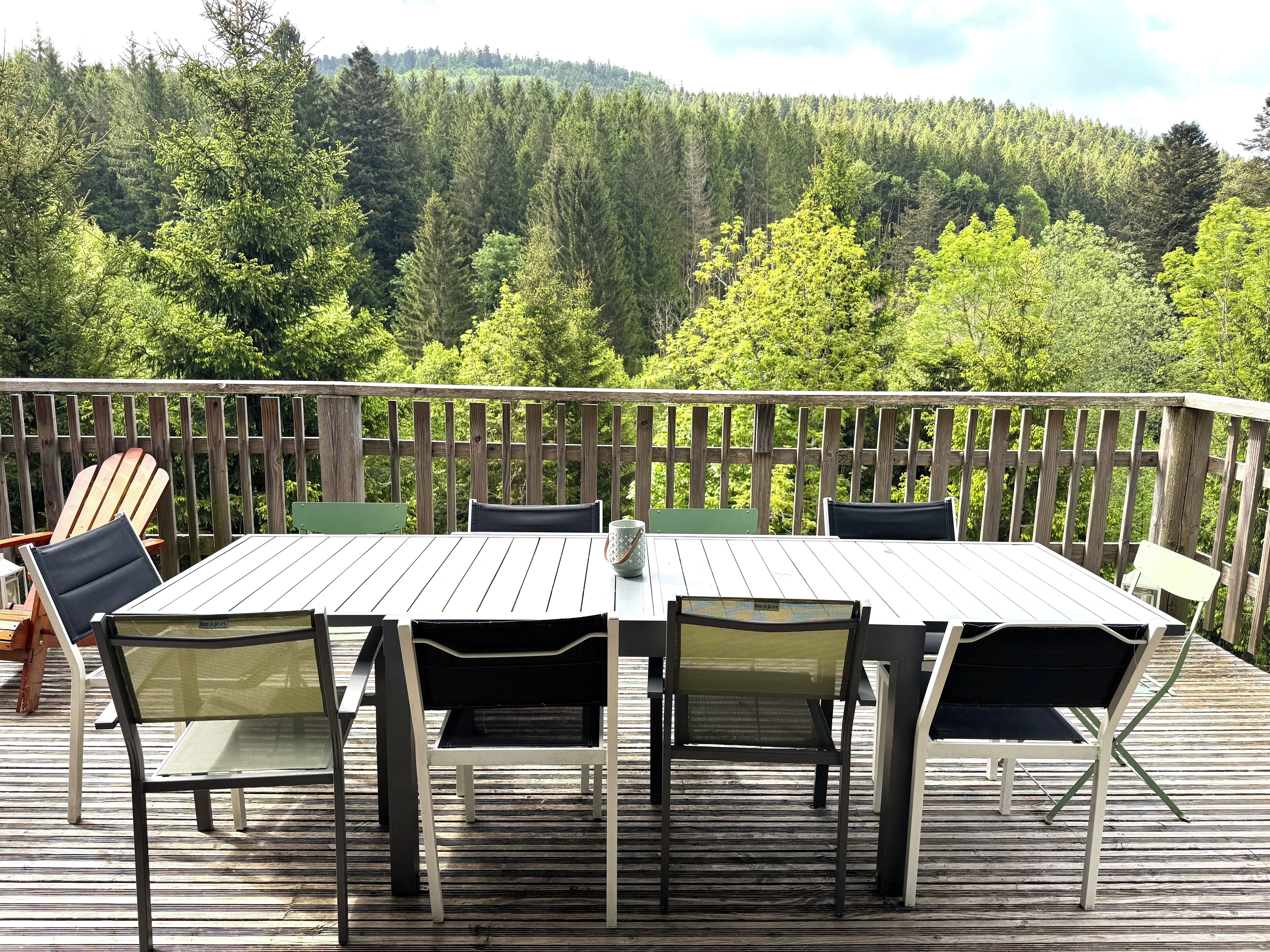 A wooden deck with a table and chairs, overlooking a forested area.