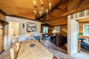 A wooden interior with a dining table, a chandelier, and a view of the kitchen and living area. - Dream cottage in the heart of nature: forest, river, cabin atmosphere & wood stove (Xonrupt-Longemer)