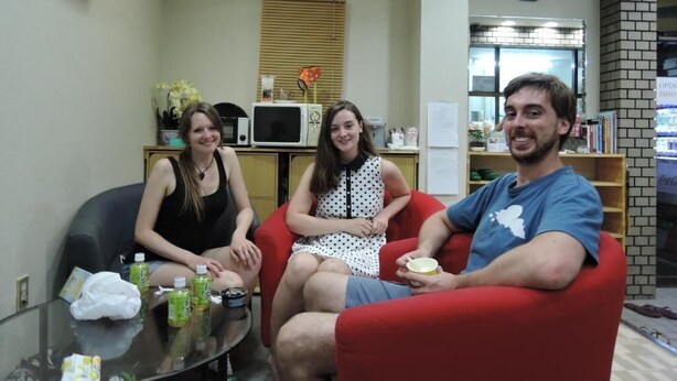 Three people seated in a room with a glass table, a microwave, and a clock on the wall. - Hotel Lucky (Osaka)