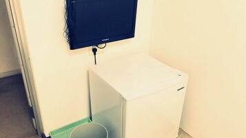 A compact room with a white washing machine, a small trash bin, and a mounted television on the wall.