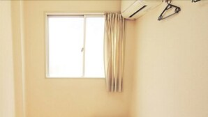 A small, clean room with a tatami mat floor, a single bed, a nightstand, and a window with curtains. - Hotel Lucky (Osaka)