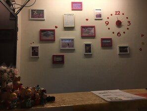 A wall with multiple framed pictures and a clock. - Shinny Inn (Kowloon)
