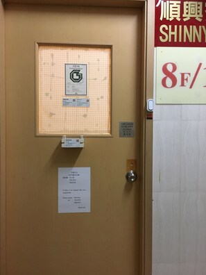 A hotel room door with a fire safety sign, a license plate, and a contact number for emergency services. - Shinny Inn (Kowloon)