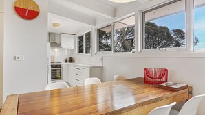 A modern kitchen with white cabinets, a wooden dining table, and a red chair. - Ski View 4 (Mount Buller)