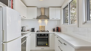 A modern kitchen with white cabinetry, a stainless steel range hood, a built-in oven, and a window providing natural light. - Ski View 4 (Mount Buller)