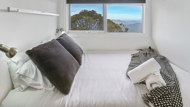 A bedroom with a bed, pillows, a window with a view of trees and mountains, and a framed picture on the wall. - Ski View 4 (Mount Buller)