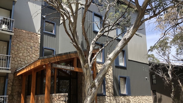 A modern building with a stone facade, a wooden entrance, and a sign reading "SNOWFALL." - Snowflake 13 (Mount Buller)