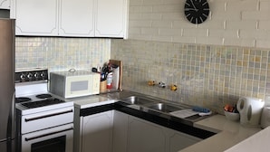 A kitchen with white cabinets, a stove, a microwave, a sink, and a clock on the wall. - Snowflake 13 (Mount Buller)