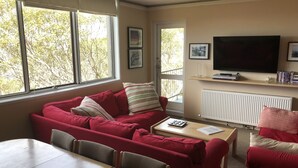 A living room with a red sofa, a TV, and a window with a view of trees. - Snowflake 14 (Mount Buller)