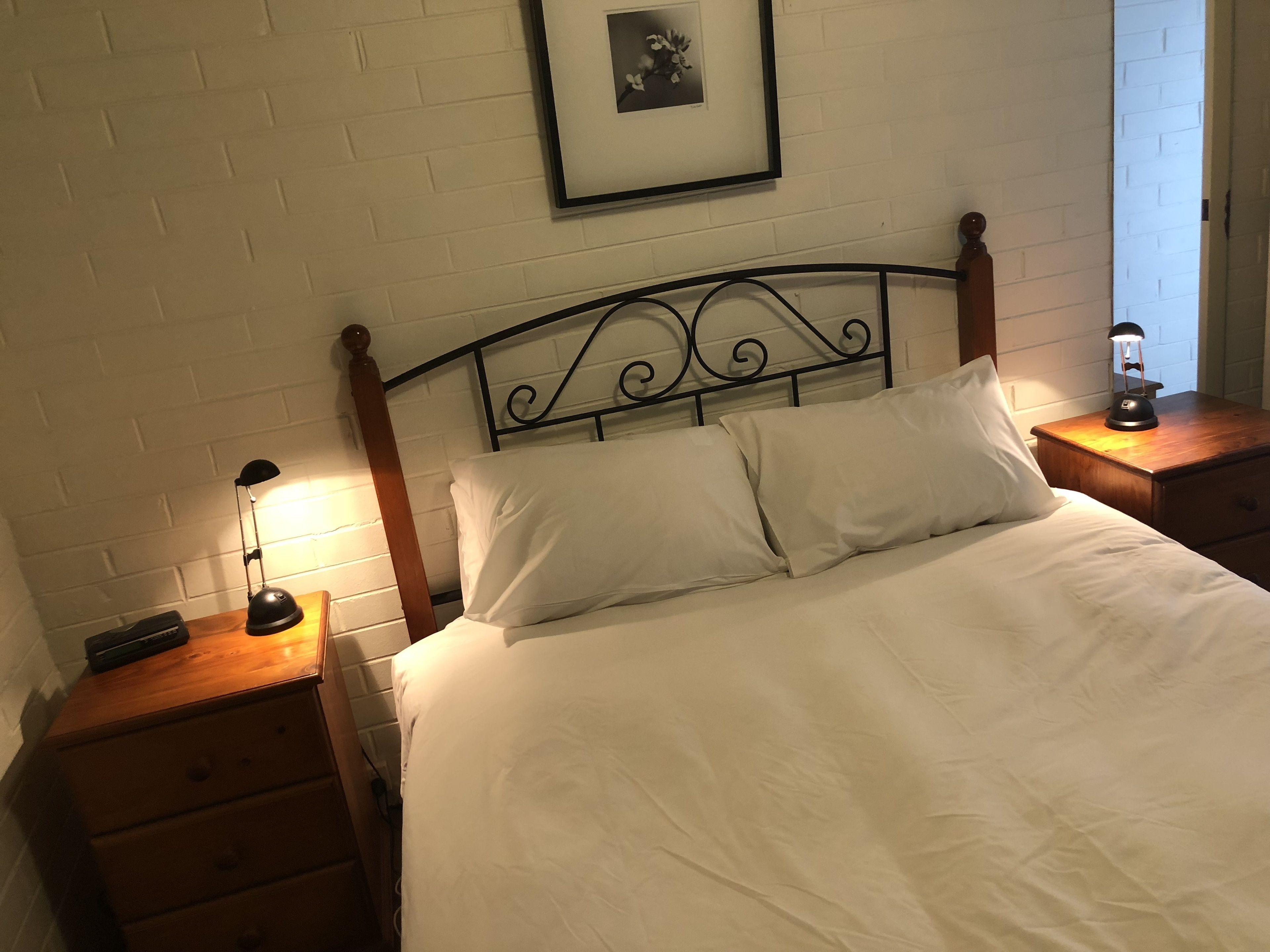 A neatly made bed with white linens, a black metal headboard, and two bedside tables with lamps.