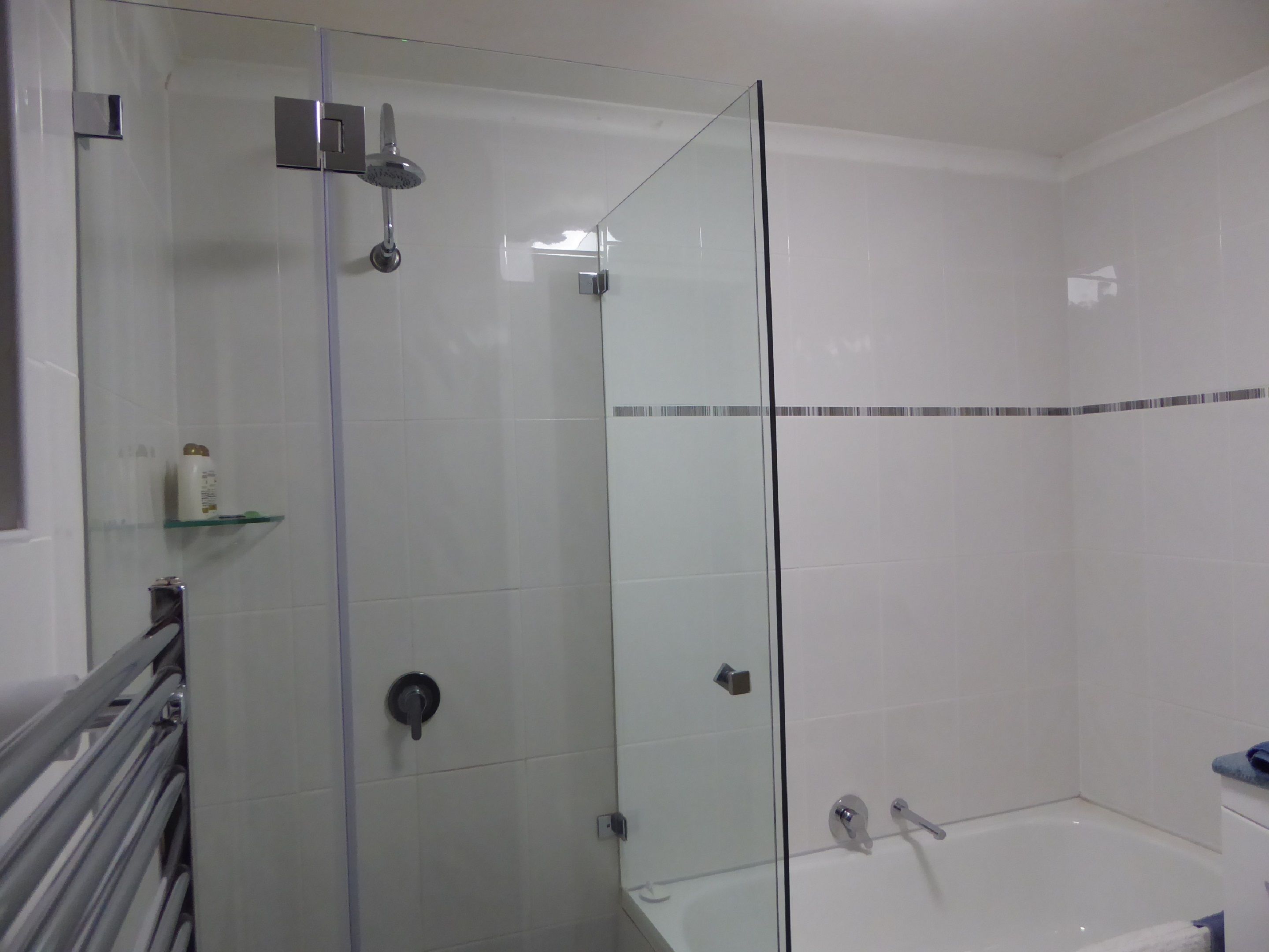 A modern bathroom with a glass shower enclosure, a bathtub, and a glass door.