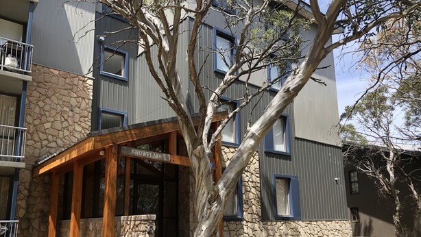 A modern building with a stone facade, a wooden entrance, and a sign reading "SNOWFALL." - Snowflake 14 (Mount Buller)