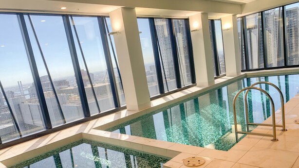 A high-rise building with a glass-enclosed infinity pool and a view of the cityscape. - Sunshine Boutique Apartments Collins (Melbourne)