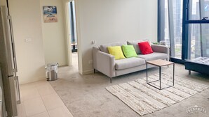 A modern living room with a grey sofa, colorful cushions, a small coffee table, and a large window offering a city view. - Sunshine Boutique Apartments Collins (Melbourne)