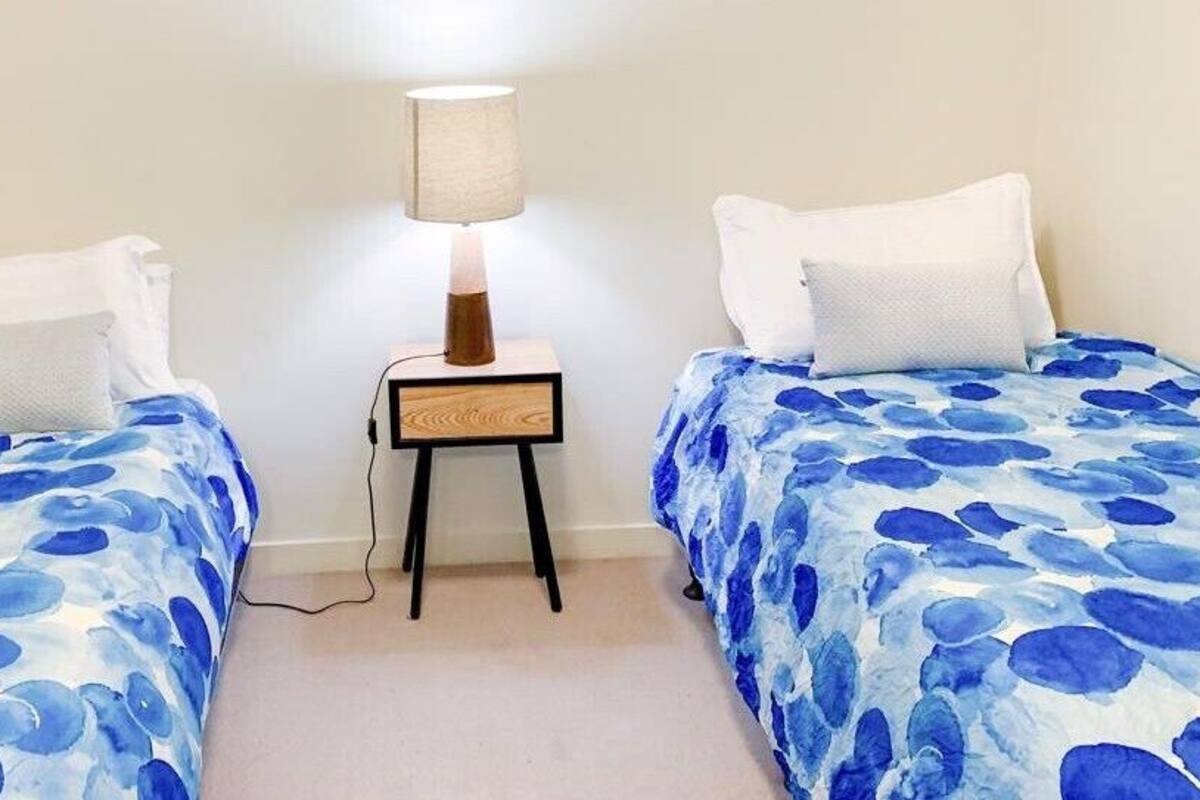 A room with two beds, each with a blue floral bedspread, a bedside table with a lamp, and white pillows.