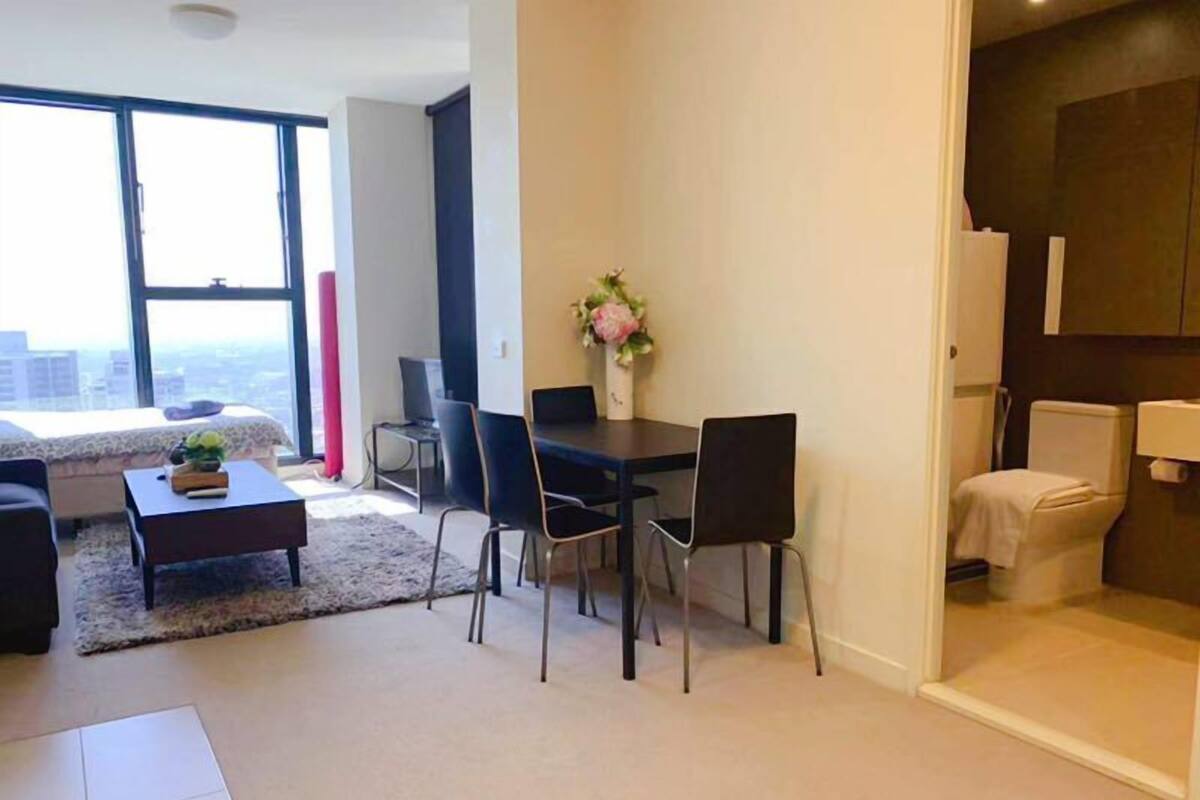 A modern living room with a large window, a dining area with a table and chairs, and a separate bathroom.