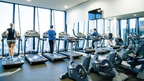 A gym with treadmills and exercise bikes, large windows, and a city view. - Sunshine Boutique Apartments Collins (Melbourne)