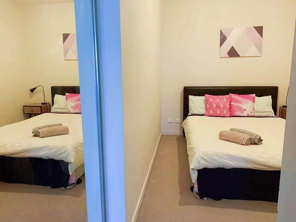 Ein Hotelzimmer mit zwei Betten, jeweils mit einem Kissen und einem zusammengerollten Handtuch.
