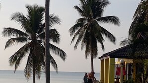 A pathway leading to a yellow building with a red awning, surrounded by palm trees and a view of the sea. - Malai Asia Resort (Thap Sakae)