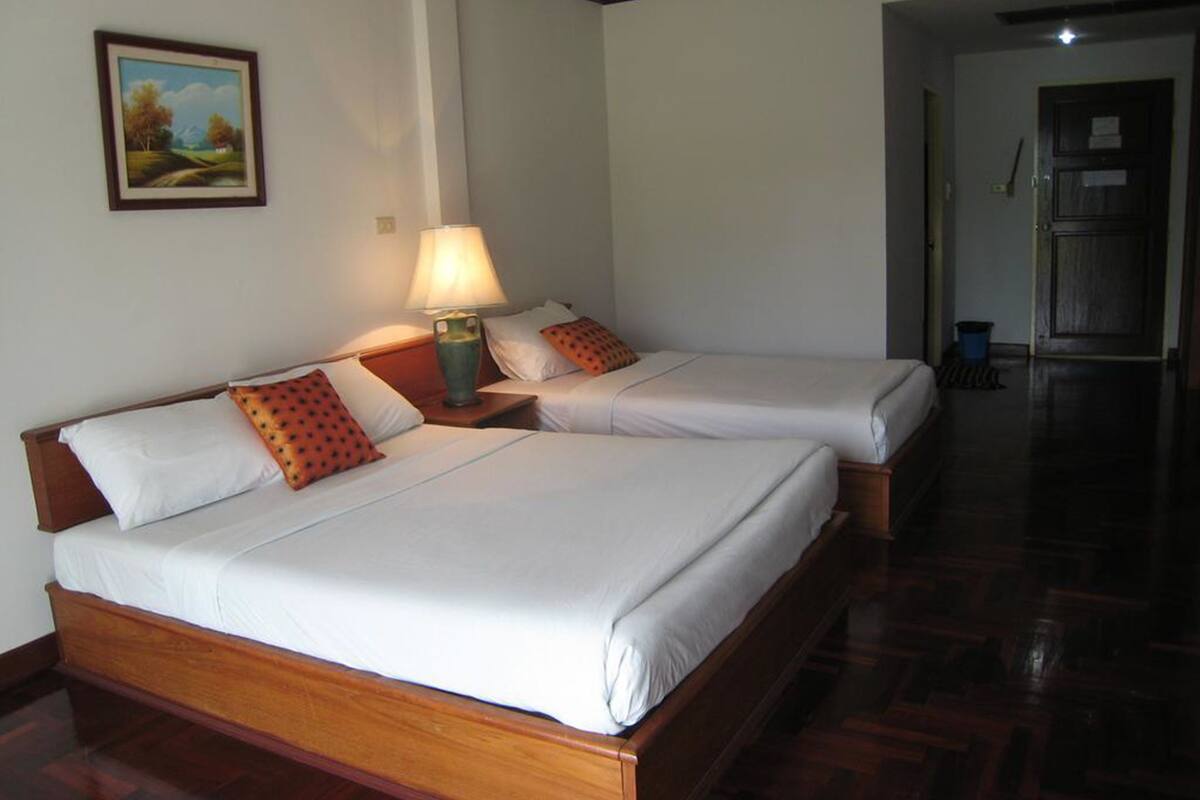 A hotel room with two single beds, a nightstand with a lamp, a painting on the wall, and a wooden floor.