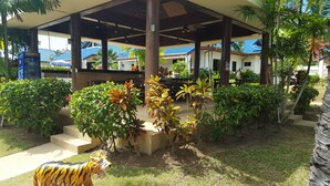 A covered outdoor area with a seating area, surrounded by lush greenery and a decorative tiger statue.