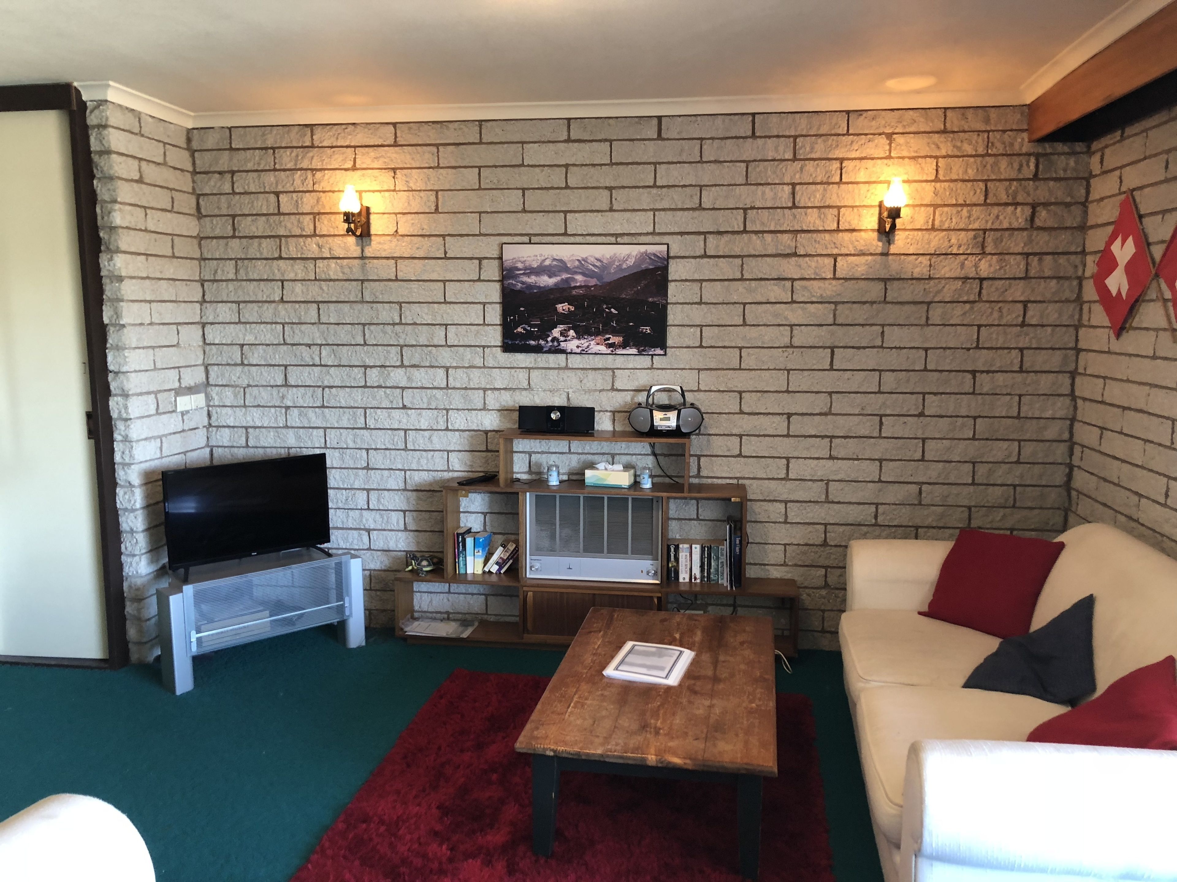 A cozy living room with a brick wall, a flat-screen TV, a vintage radio, and a bookshelf.